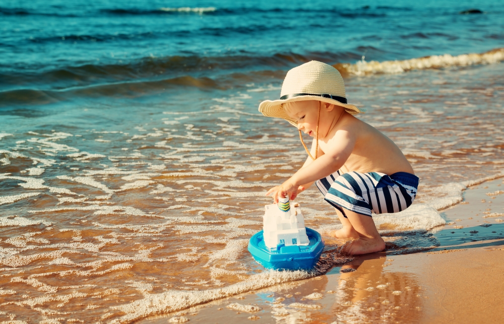 Malý kluk hrající si na pláži s lodičkou