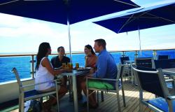 Celebrity Xpedition - Celebrity Cruises - lidé sedící u stolu ve venkovních prostorech restauraci na lodi pod modrým slunečníkem